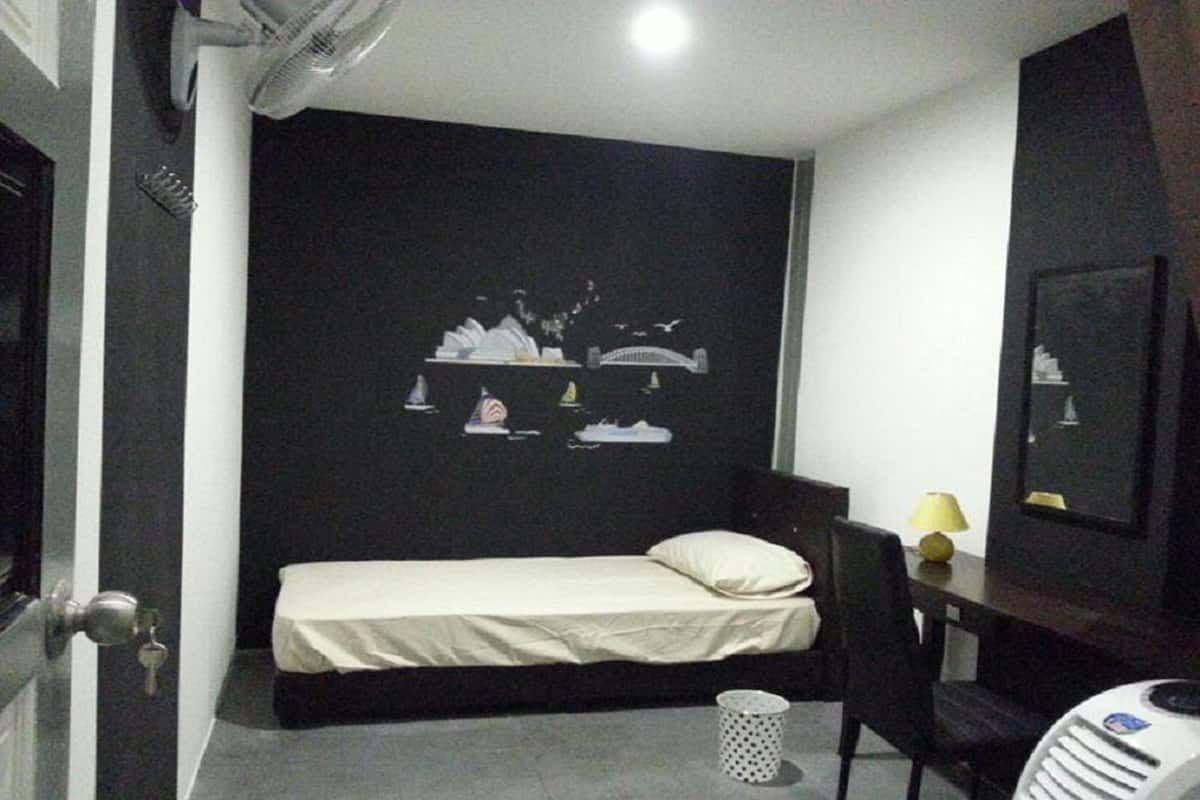 A small, dimly lit room with a single bed, a desk with a lamp, and a wall-mounted TV.