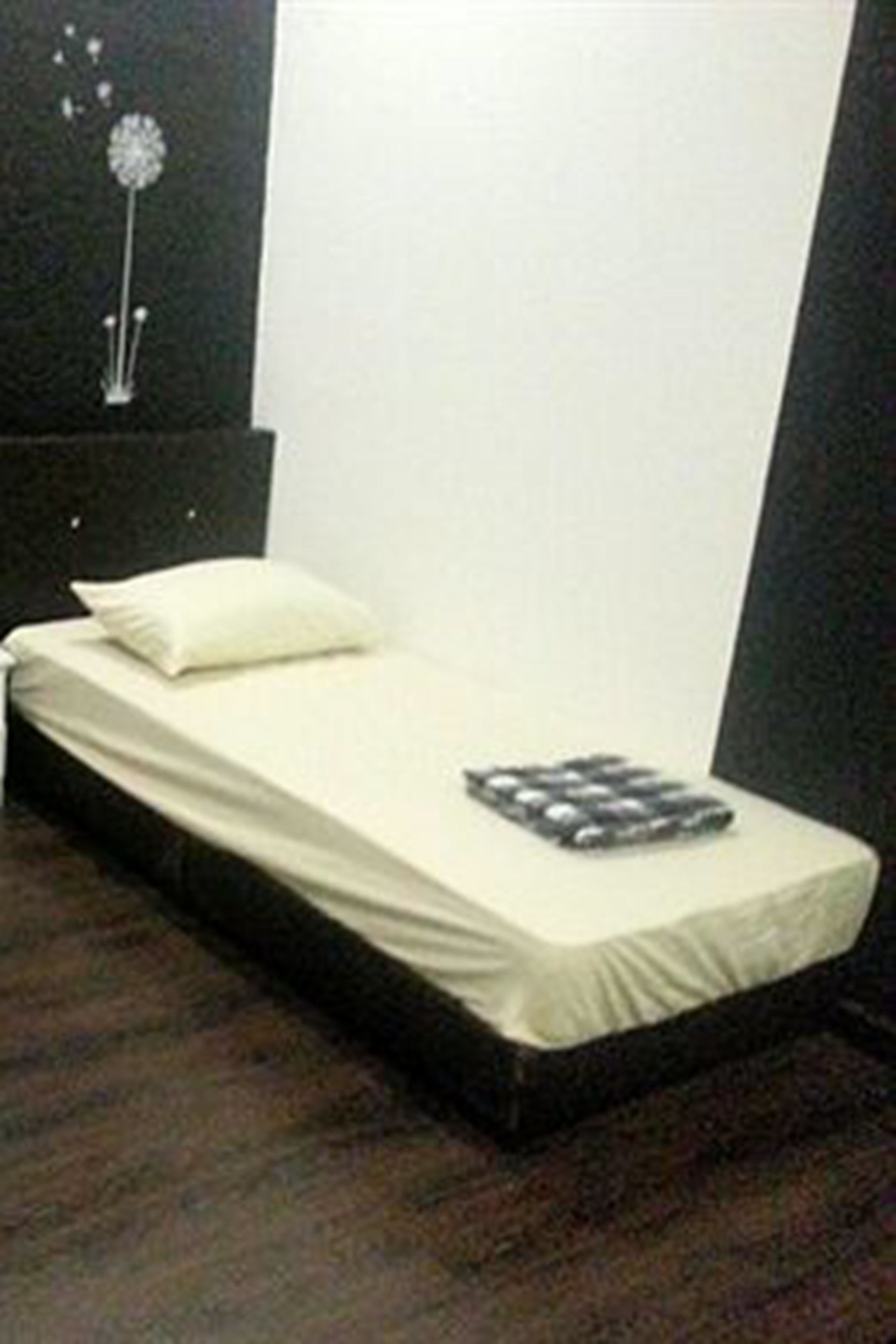 A single bed with a white mattress and a pillow, a bedside table with a lamp, and a wall decoration.
