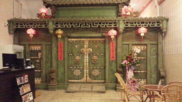 A traditional Chinese gate with intricate designs and red decorations, a reception desk with magazines, and wicker chairs in the foreground. - Kimberley House (George Town)