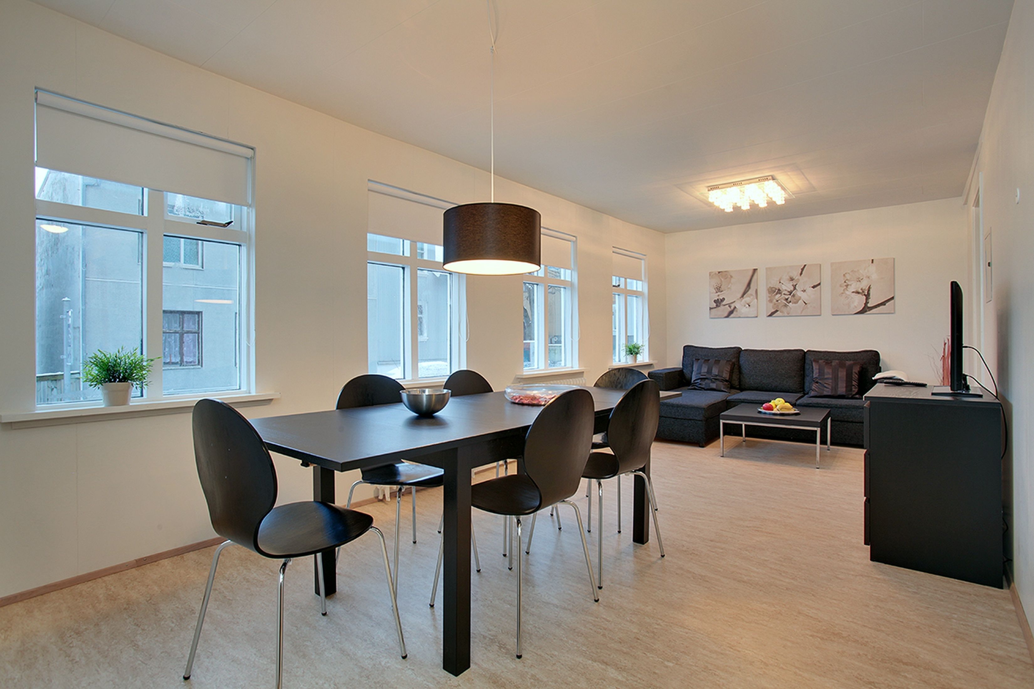 A modern living room with a dining area, large windows, and a black sofa.