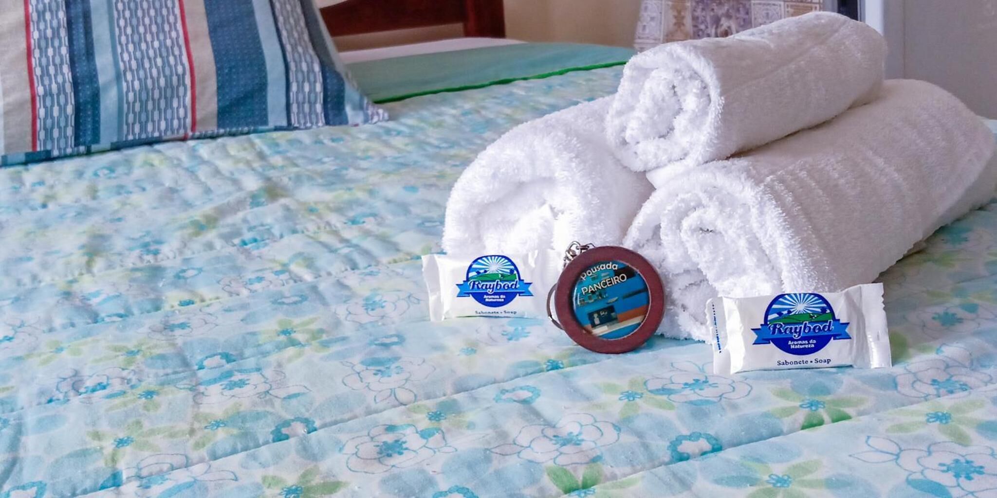 Ein Bett mit einem blumigen Bettbezug, zwei aufgerollte weiße Handtücher und zwei Seifen- sowie Shampoo-Proben.