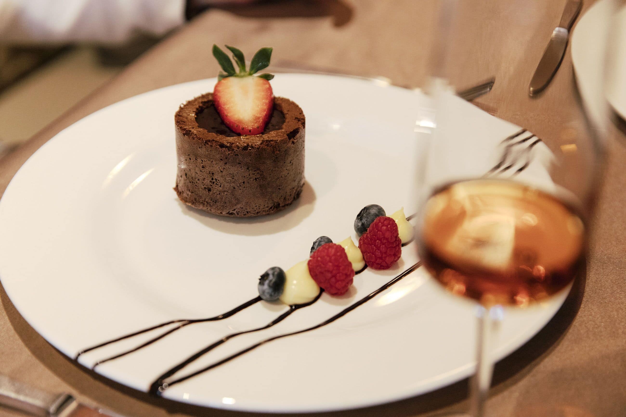 A dessert plate with a chocolate cake, strawberries, raspberries, and blueberries, and a glass of wine.