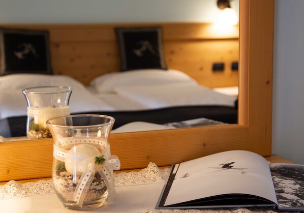 A neatly made bed with a wooden headboard, a glass with a decorative ribbon, and a book on a lace-trimmed table. - Hotel Astoria  (Primiero San Martino di Castrozza)