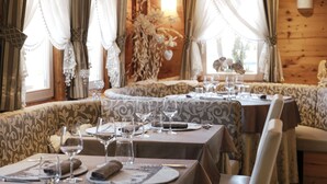 Uma área de refeições com mesas postas para uma refeição, com toalhas de mesa estampadas e decoração rústica em madeira.