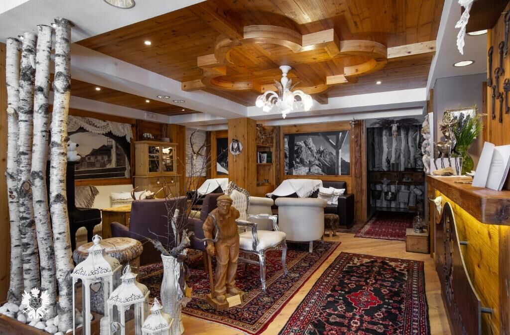 A room with wooden ceiling beams, a chandelier, a patterned rug, and a statue.