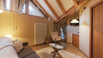 A cozy room with a sofa, a glass coffee table, a chair, a radiator, and a wooden ceiling.