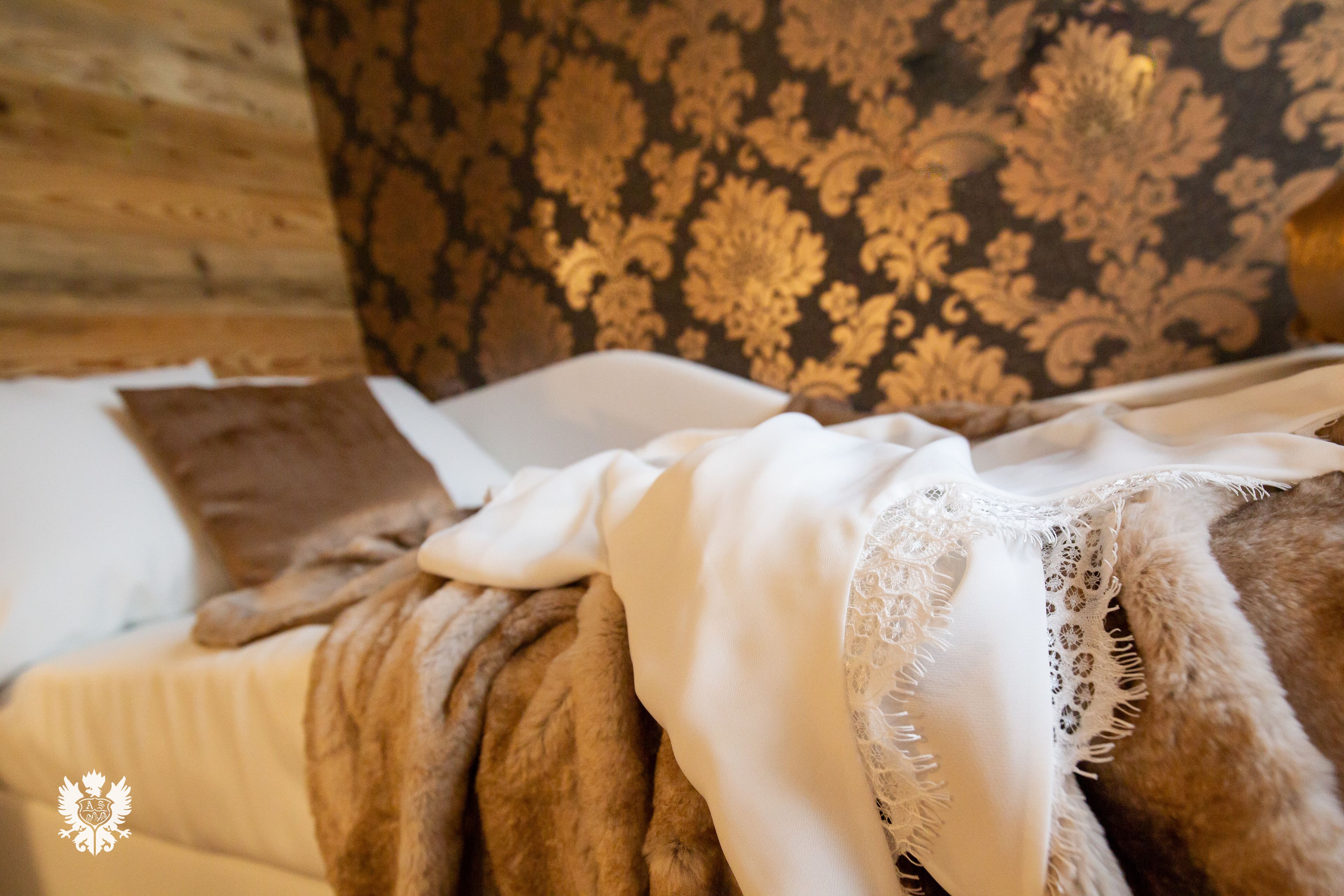 A bed with a brown blanket, white pillows, and a lace-trimmed white throw.