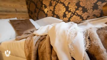 A bed with a brown blanket, white pillows, and a lace-trimmed white throw.
