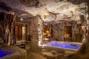 Een wellnessruimte met een jacuzzi, houten meubels en een rustieke, grotachtige inrichting.