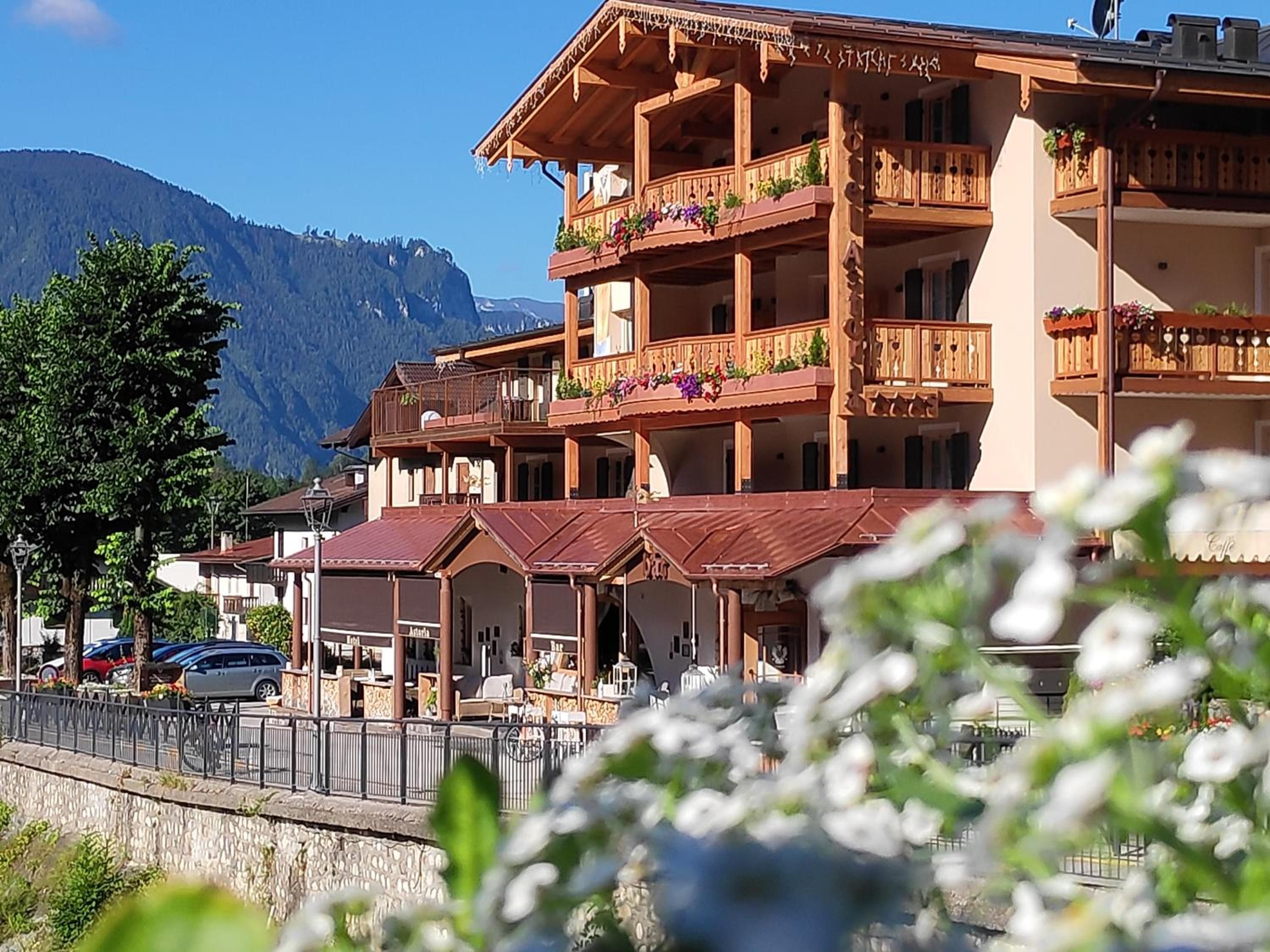 A multi-story wooden building with balconies, a stone wall, and a mountain in the background.