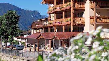 A multi-story wooden building with balconies, a stone wall, and a mountain in the background.