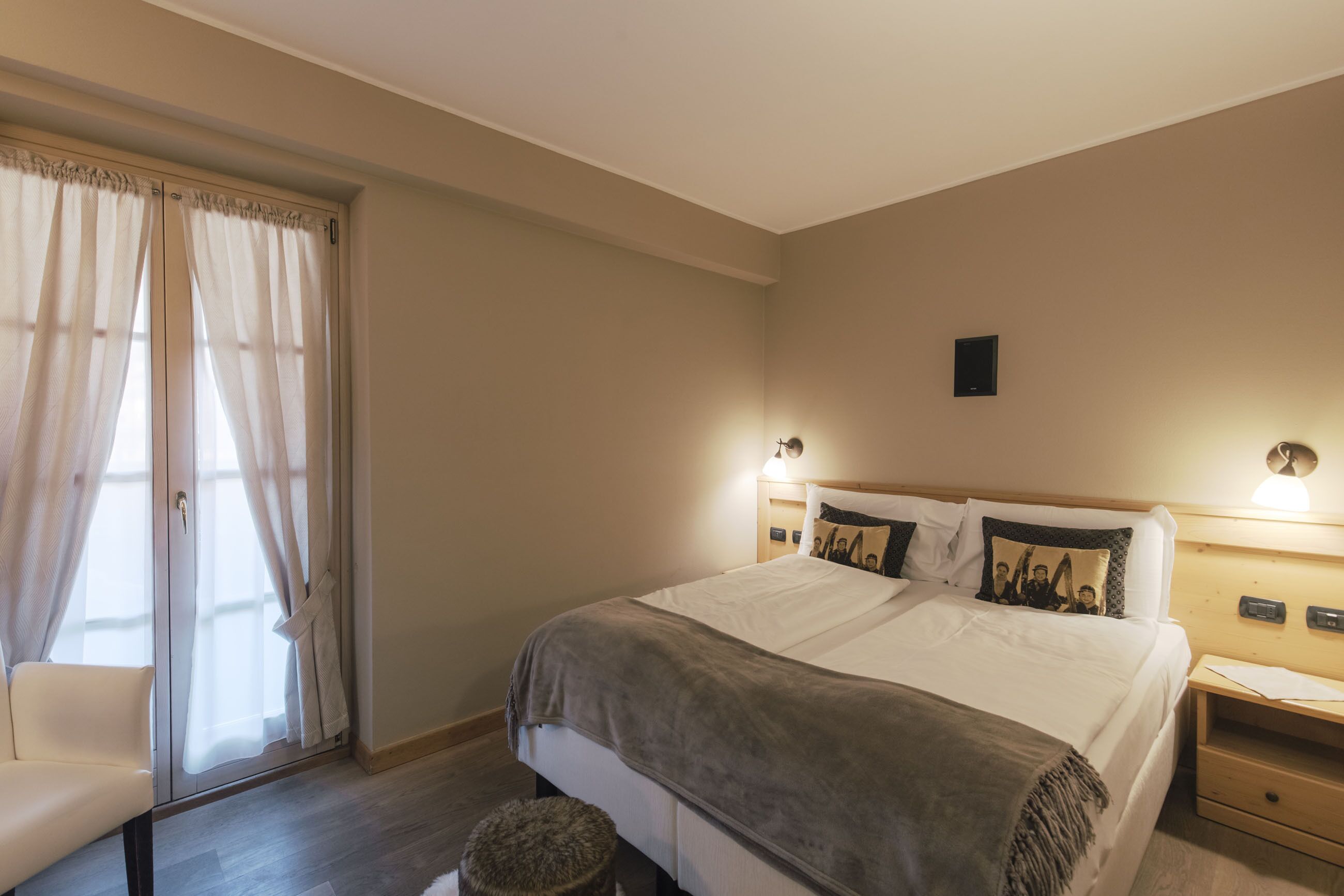 Een slaapkamer met een bed, een stoel, een nachtkastje, een lamp en een raam met gordijnen.