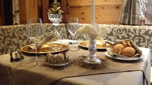 A dining table set with plates, glasses, and a candle, with a decorative figure and a candle holder in the background. - Hotel Astoria  (Primiero San Martino di Castrozza)