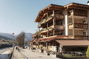 Un edificio de varios pisos con balcones, un área de estar al aire libre techada y una vista de un río y montañas al fondo.