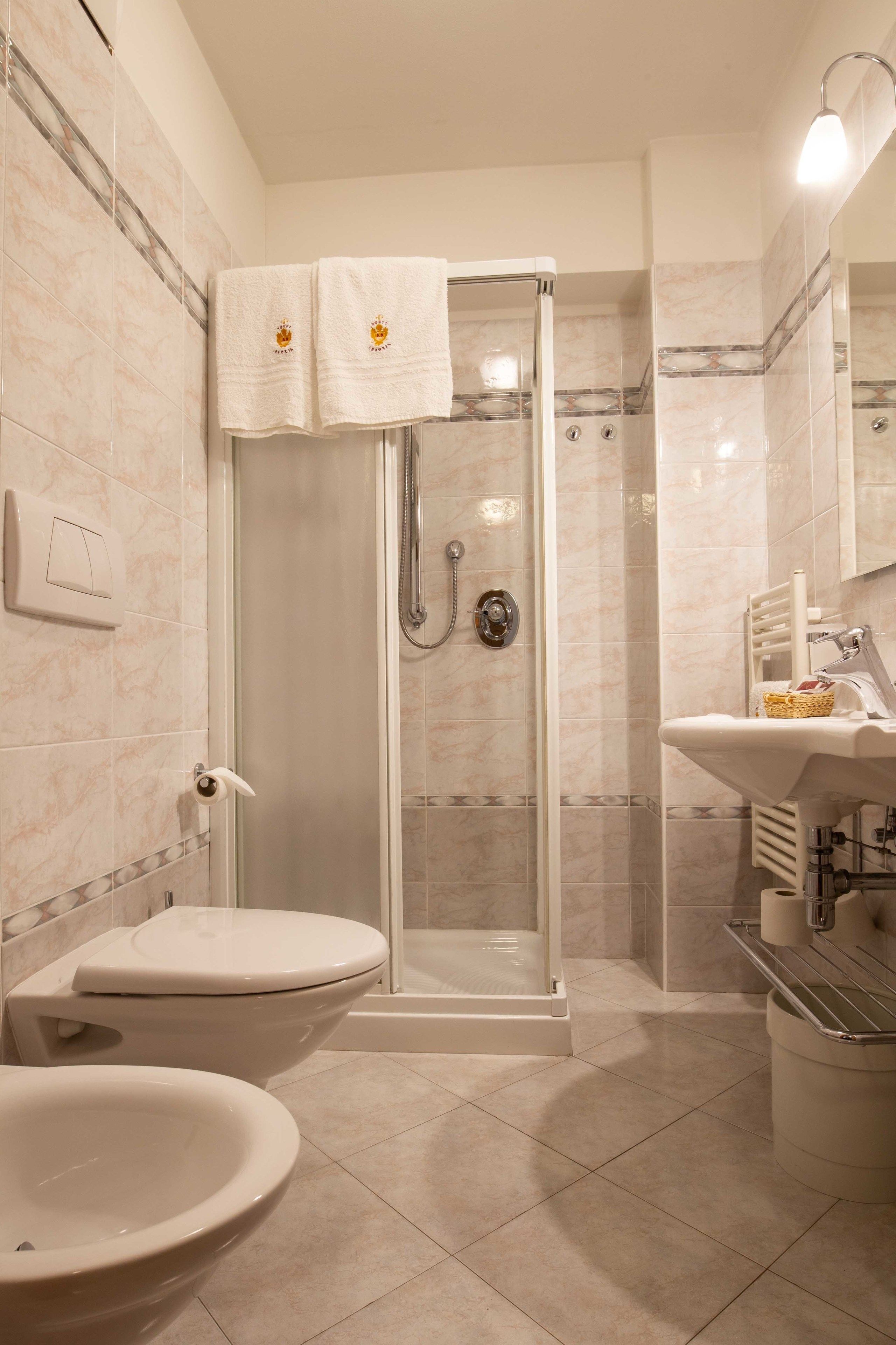 A bathroom with a glass-enclosed shower, a toilet, and a sink with a basket of toiletries.