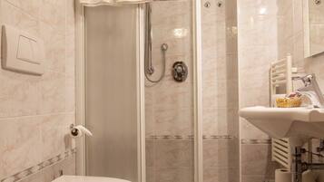 A bathroom with a glass-enclosed shower, a toilet, and a sink with a basket of toiletries.