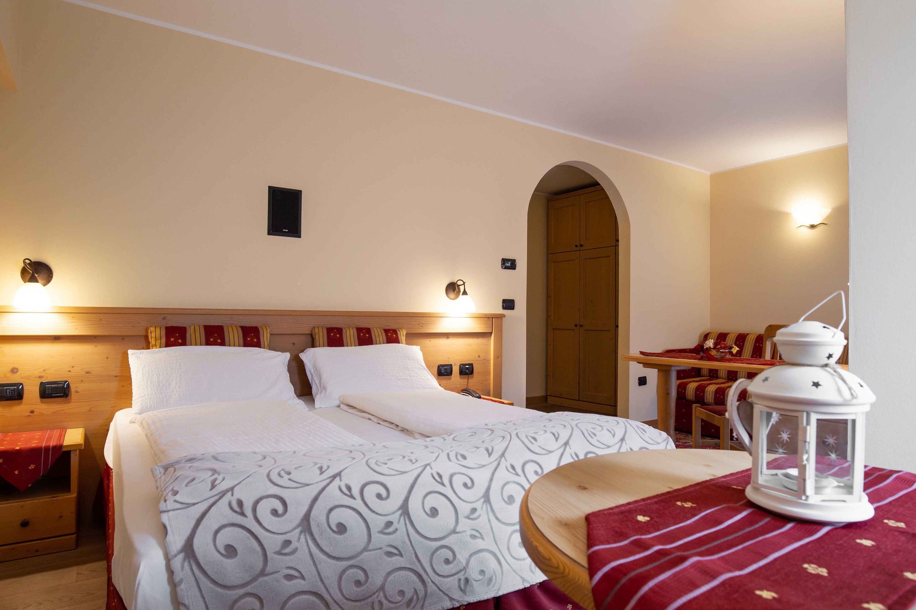 Siististi järjestetty hotellihuone, jossa on sänky, yöpöydät, pieni pöytä tuolilla sekä koristeellinen lyhty.