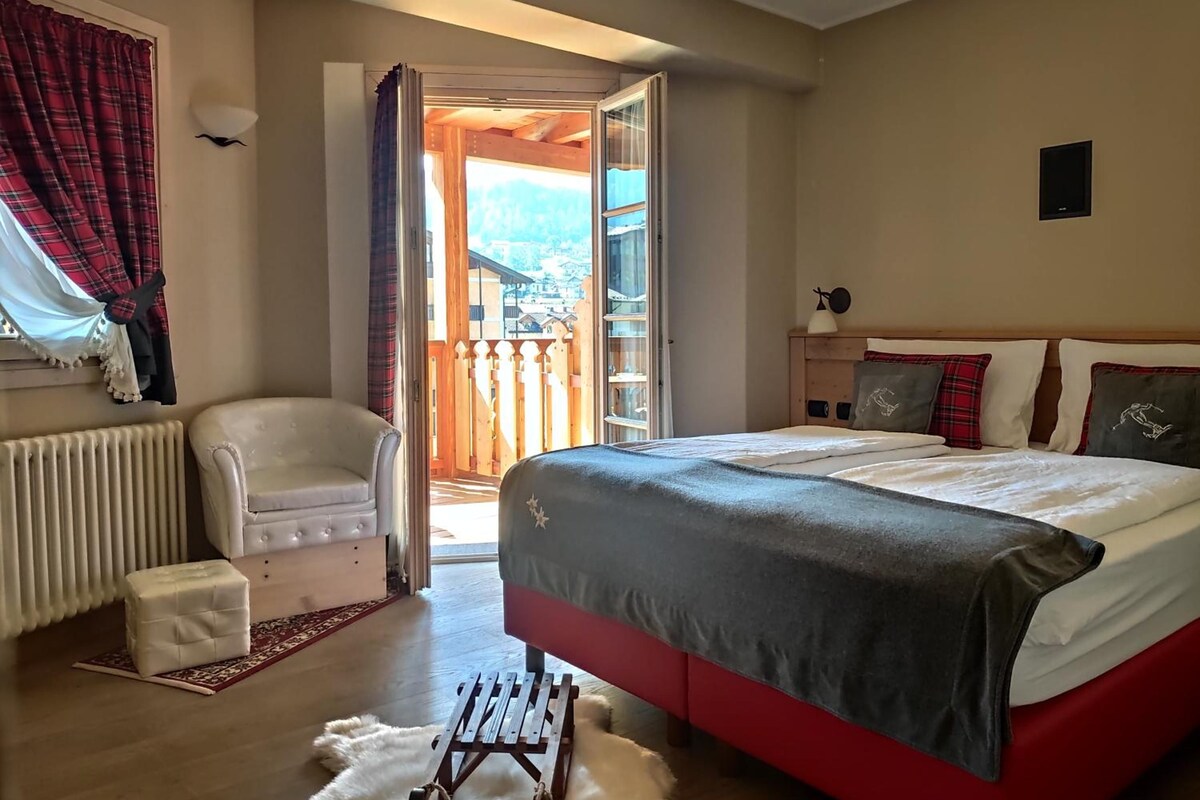 Un dormitorio con cama, una silla, un radiador y vistas al exterior.