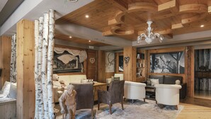 A cozy room with wooden walls, a fireplace, a sofa, and a dining area. - Hotel Astoria  (Primiero San Martino di Castrozza)