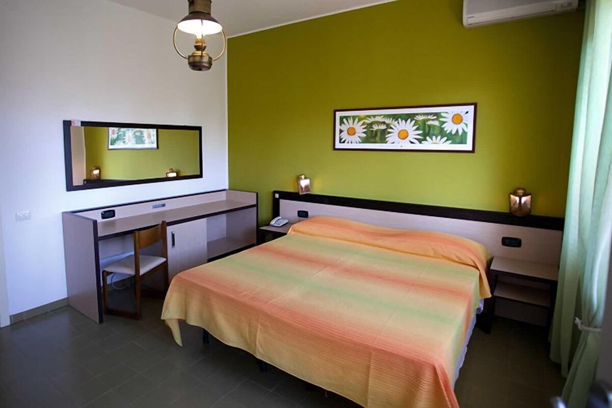 Un dormitorio con cama, escritorio, silla, espejo y un cuadro en la pared.