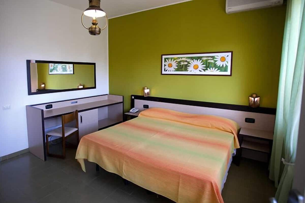 A bedroom with a bed, a desk, a chair, a mirror, and a painting on the wall.