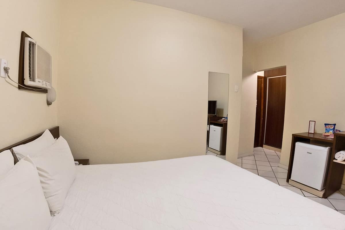 Een hotelkamer met een bed, een kleine koelkast, een televisie en een spiegel aan de muur.