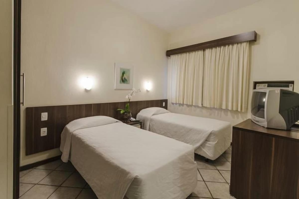 Ein Hotelzimmer mit zwei Betten, einem Schreibtisch, einem Fernseher und einem fenster mit Vorhängen.