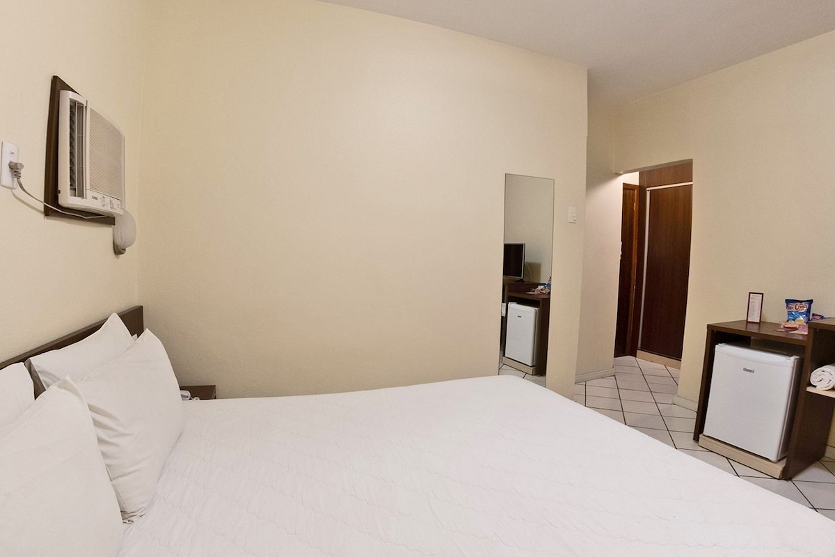 Ein Hotelzimmer mit einem Bett, einem kleinen Kühlschrank, einem Fernseher und einem Spiegel an der Wand.