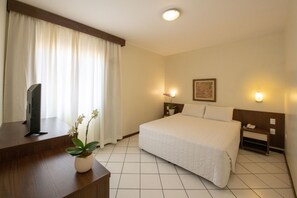 A hotel room with a bed, a desk with a TV, a potted plant, and two bedside lamps. - Hotel Ryan (Balneário Camboriú)