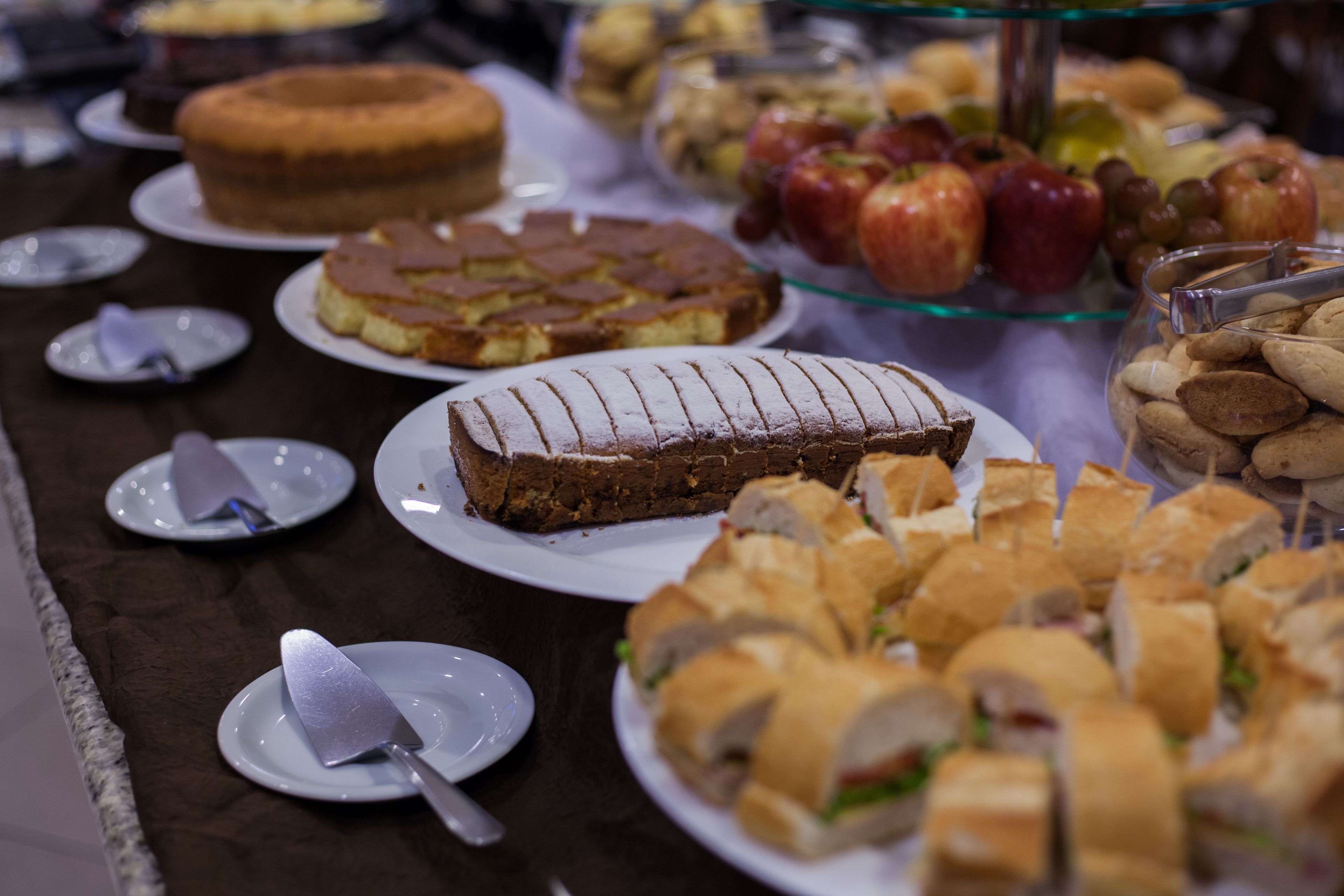 A buffet table with various food items including cakes, sandwiches, and fruits.