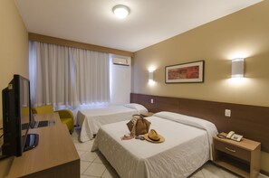 A hotel room with two beds, a desk with a computer, a chair, a bedside table with a phone, and a wall-mounted light. - Atobá Praia Hotel (Balneário Camboriú)