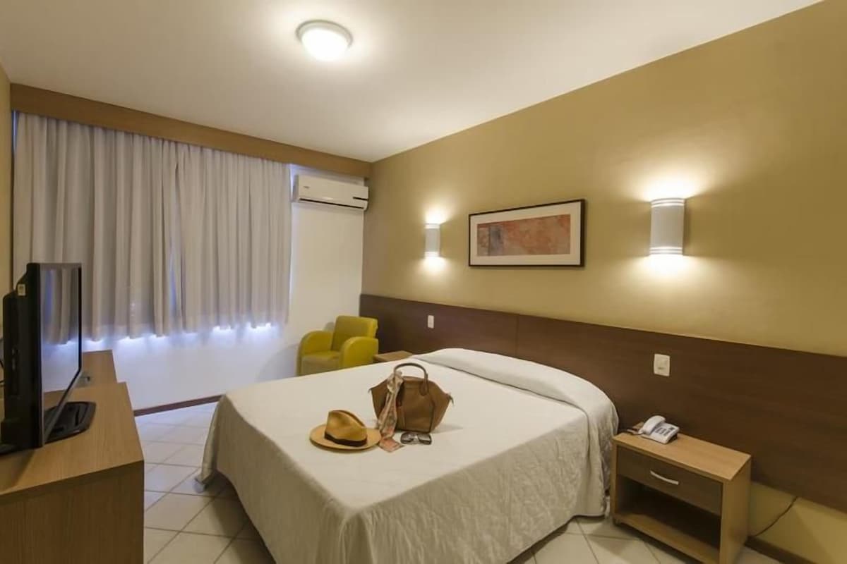 A hotel room with a bed, a desk, a chair, a television, and a window with curtains.