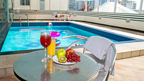 A poolside table with a drink, fruit, and a towel. - Atobá Praia Hotel (Balneário Camboriú)