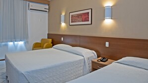 A hotel room with two beds, a bedside table with a phone, a wall-mounted air conditioner, and a framed artwork. - Atobá Praia Hotel (Balneário Camboriú)