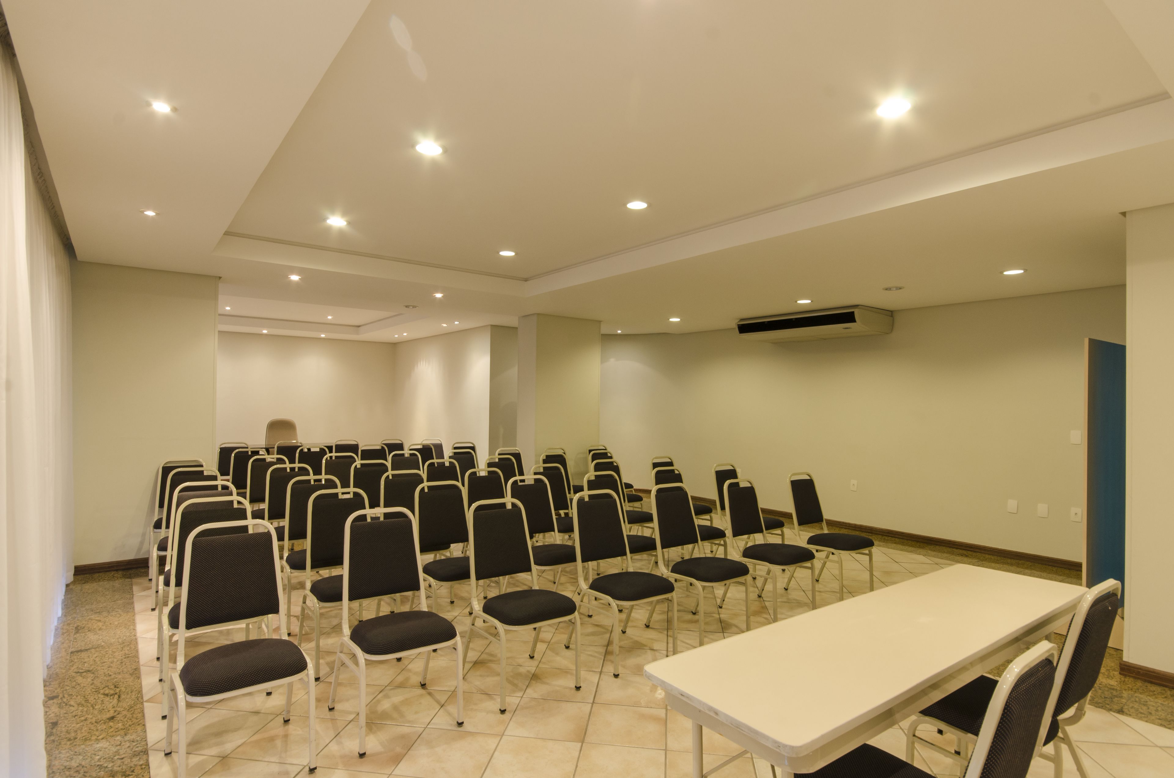 A conference room with rows of chairs, a long table, and recessed ceiling lights.