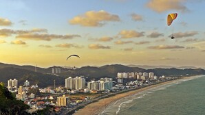 A coastal cityscape with a beach, high-rise buildings, and two paragliders. - Atobá Praia Hotel (Balneário Camboriú)