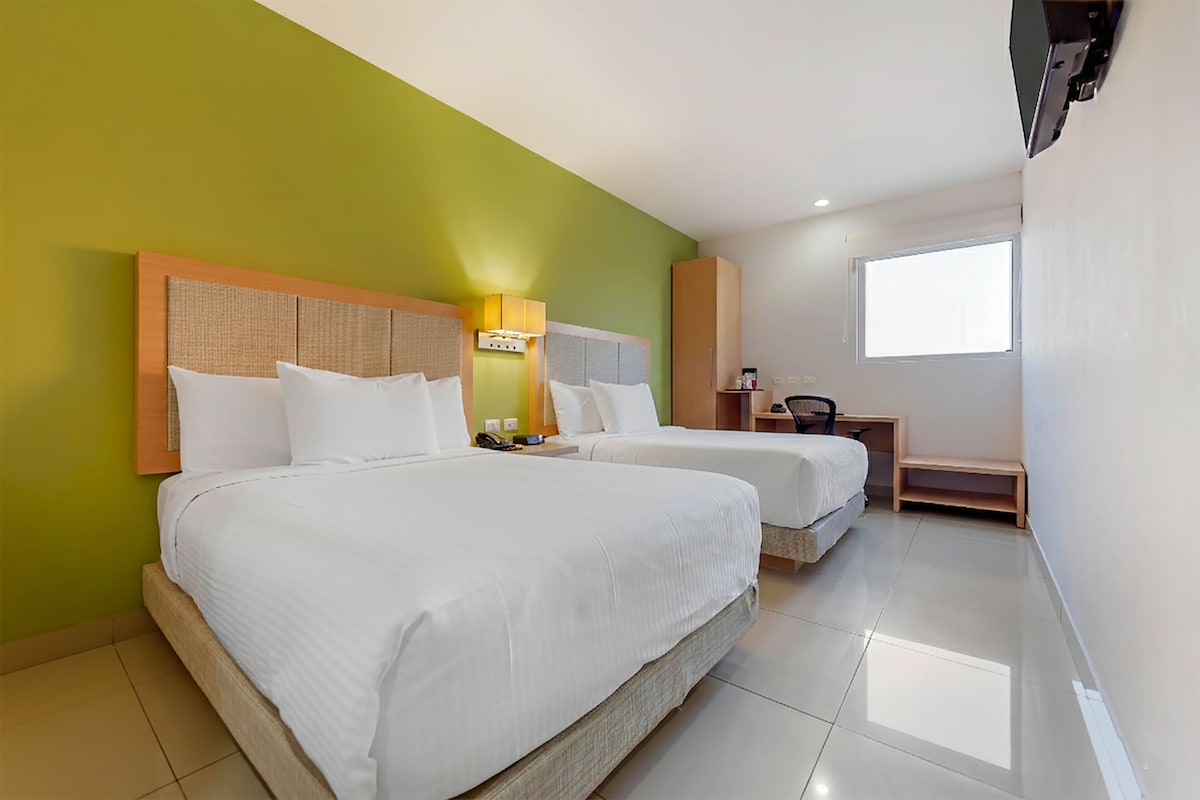 A hotel room with two beds, a desk, a chair, a television, and a window.