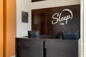 Una mesa de recepción con un letrero que dice 'Sleep INN', dos sillas negras y una computadora Dell.