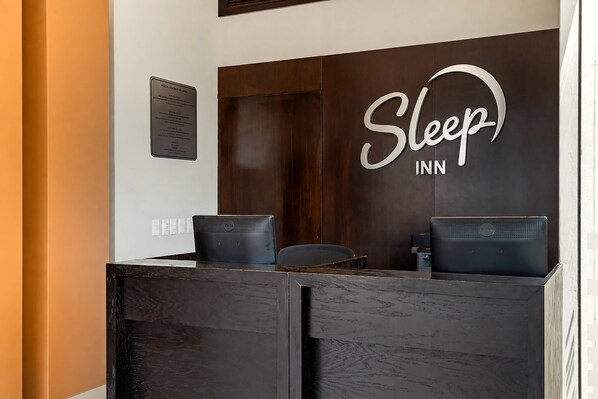 Una mesa de recepción con un letrero que dice 'Sleep INN', dos sillas negras y una computadora Dell.