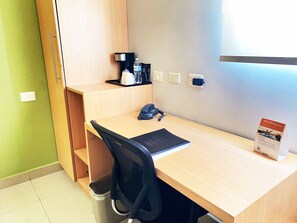 A small office space with a desk, chair, and a trash bin. There is a water bottle, a phone, and a coffee machine on the desk. - Sleep Inn Culiacan (Culiacán)