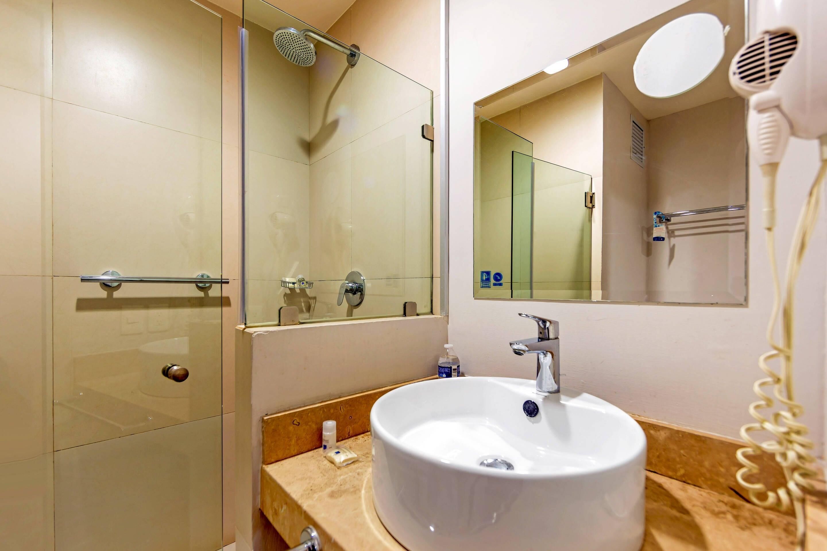 A modern bathroom with a glass shower enclosure, a sink with a mirror above it, and a hairdryer on the wall.