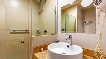 A modern bathroom with a glass shower enclosure, a sink with a mirror above it, and a hairdryer on the wall.