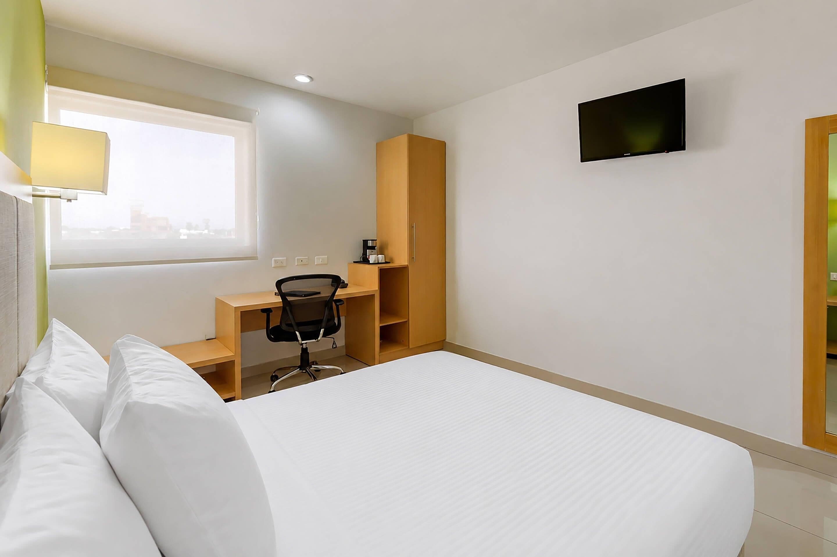 A hotel room with a bed, a desk with a chair, a television, and a window.