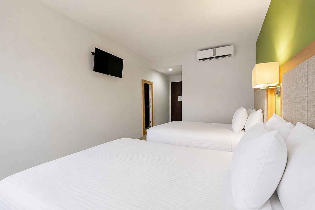 Habitación de hotel con dos camas, un televisor de pantalla plana en la pared, un aire acondicionado y una lámpara de noche.