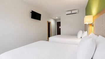 A hotel room with two beds, a flat-screen TV mounted on the wall, an air conditioning unit, and a bedside lamp.