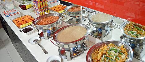 A buffet with various food options including fruits, cereals, and dishes in metal containers.