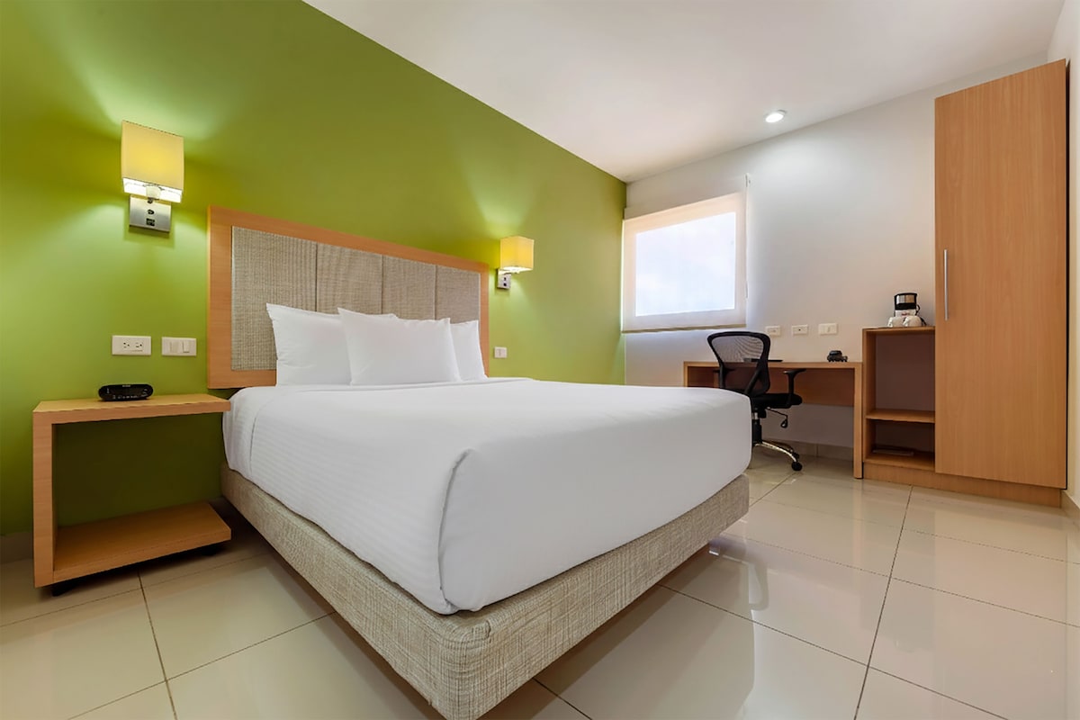 A hotel room with a large bed, a desk, and a wardrobe.