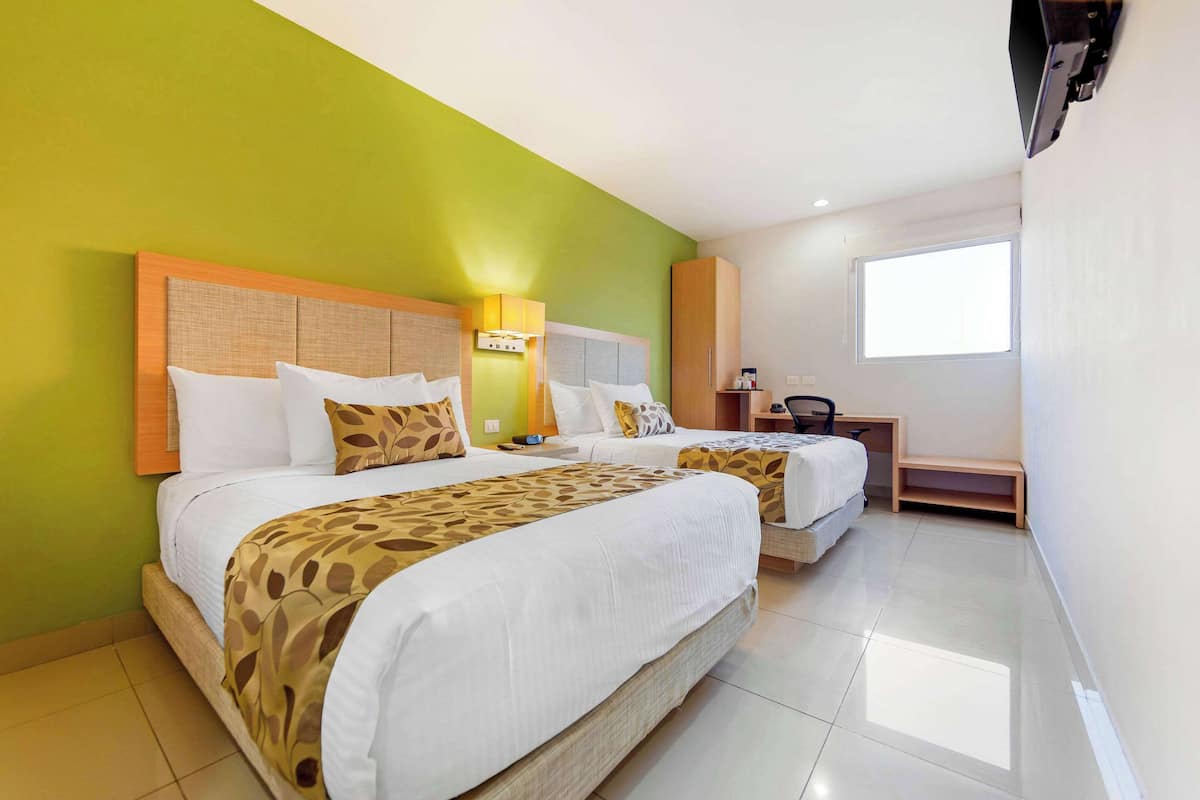 A hotel room with two beds, a small desk, and a window.