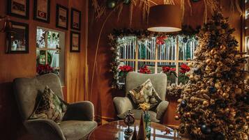 A cozy room with a Christmas tree, two armchairs, a round table with a decorative item, and framed pictures on the wall.