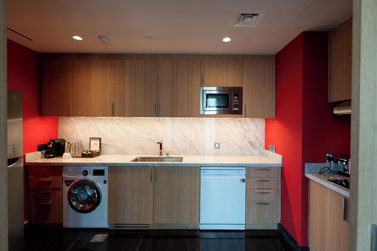 A compact kitchen with wooden cabinets, a built-in microwave, a washing machine, and a dishwasher.